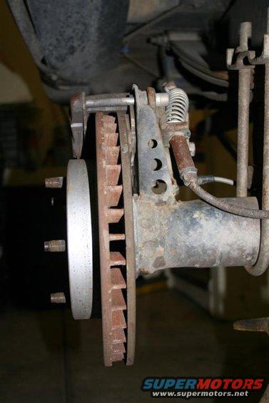 Rear brake rotor and caliper assembly with rusty rotor and visible brake pads