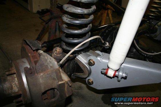 Close-up of a vehicle's front suspension with a rusty brake caliper, coil spring, and white shock absorber