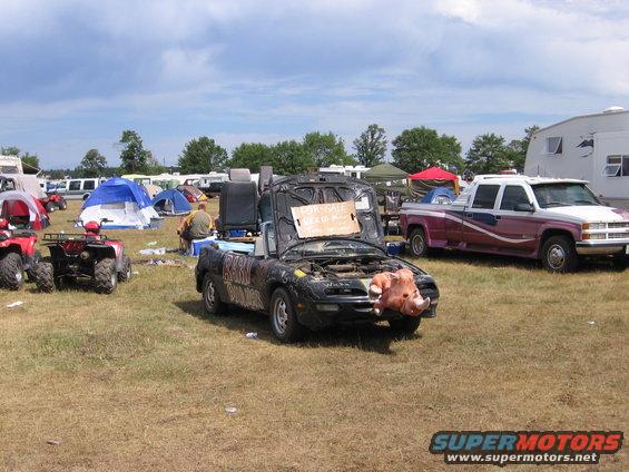 modified black convertible with pig nose, "FOR SALE" sign on hood, parked in a field with tents and ATVs