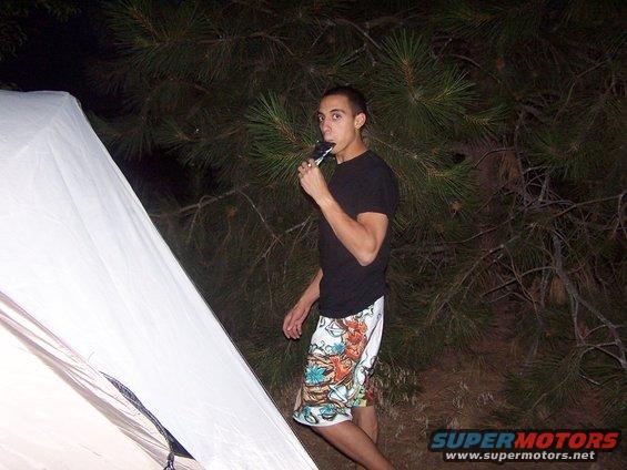 Man eating a popsicle next to a white tent in a wooded area