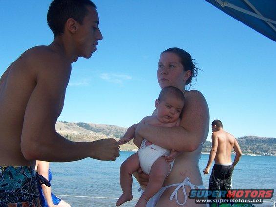 Man and woman holding a baby on a beach with another man in the background