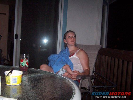 Woman holding baby on porch chair, glass table with container and drink in foreground