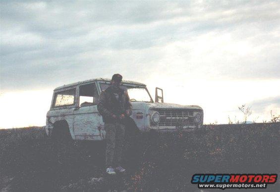 Man in camouflage stands by a white 1978 Ford Bronco with a dented front end