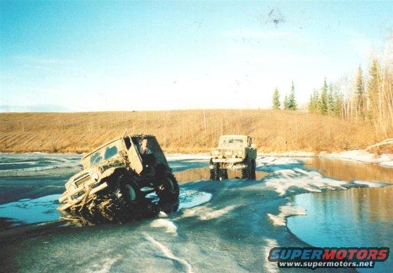 Two off-road vehicles driving through icy water, one tilted