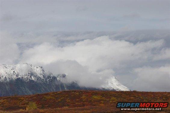Mountain landscape with snow-capped peaks and autumn foliage under cloudy sky