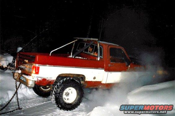 red and white pickup truck with roll bar in snow, exhaust smoke visible