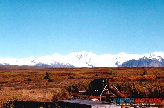Landscape with snow-capped mountains, autumn tundra, and a rustic structure with a slide