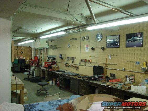 Garage workshop with tools on pegboard walls, workbenches, and two framed car photos
