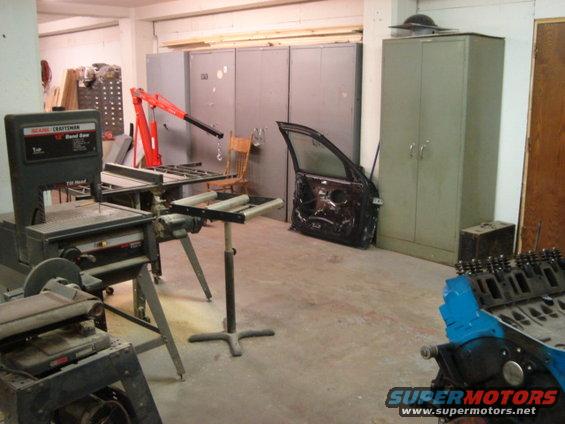 Car door leaning against a wall in a workshop with tools and an engine block