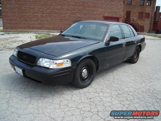 Dark green 2000 Ford Crown Victoria sedan with black grille and steel wheels, parked on cracked asphalt