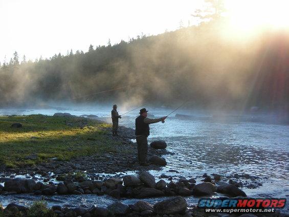 Two men fishing in a misty river with sunbeams breaking through the fog