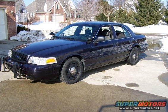 Dark blue Ford Crown Victoria police car with a push bumper parked in a driveway with snow on the ground