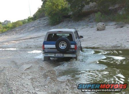 1996 Ford Bronco driving through shallow water on a dirt path