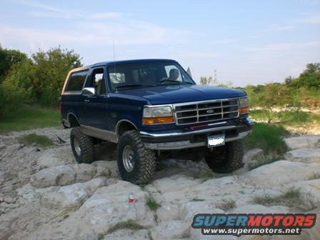 Blue 1996 Ford Bronco with lifted suspension driving over large rocks