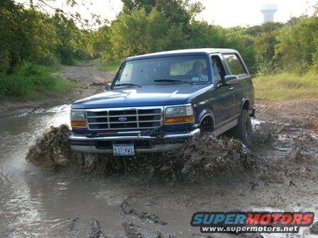 Blue Ford Bronco splashing through mud on a dirt road. License plate reads 531-VWL