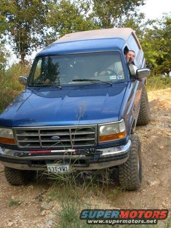 Blue 1996 Ford Bronco with lifted suspension driving on a dirt trail