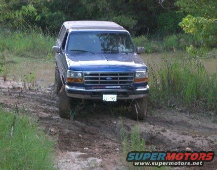 Blue Ford Bronco with a license plate reading "537 VWD" driving through mud and water