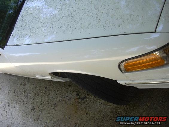 Front fender and tire of a white sedan, possibly a 1997 Ford Crown Victoria