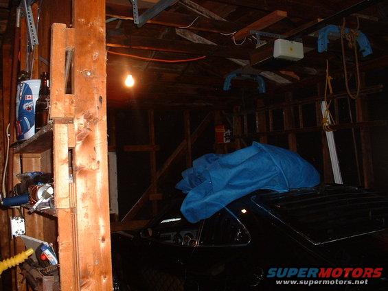 Black 1978 Ford Mustang II coupe covered with a blue tarp in a garage, side view