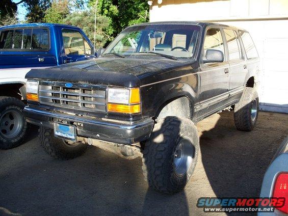 Black Ford Explorer SUV with lifted suspension and large tires, parked next to a blue pickup truck