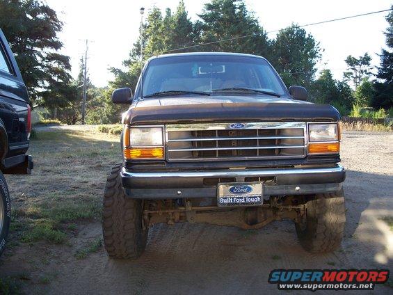 Front view of a lifted 1990 Ford Explorer with large tires. Another vehicle is partially visible on the left. "Built Ford Tough" plate is on the bumper