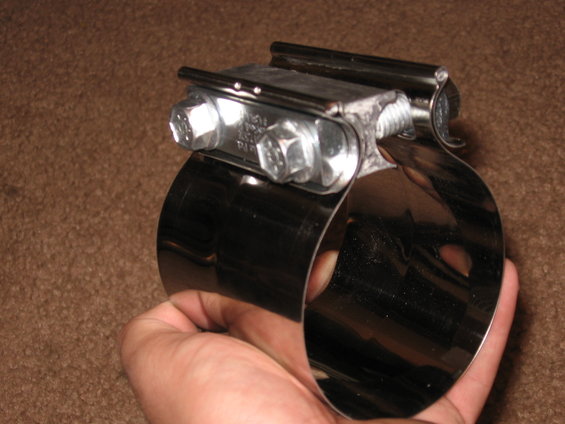 Close-up of a shiny metal exhaust clamp with two bolts being held in a hand