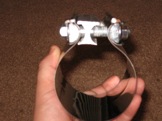 Metal hose clamp with bolt and nut held in hand over brown carpet