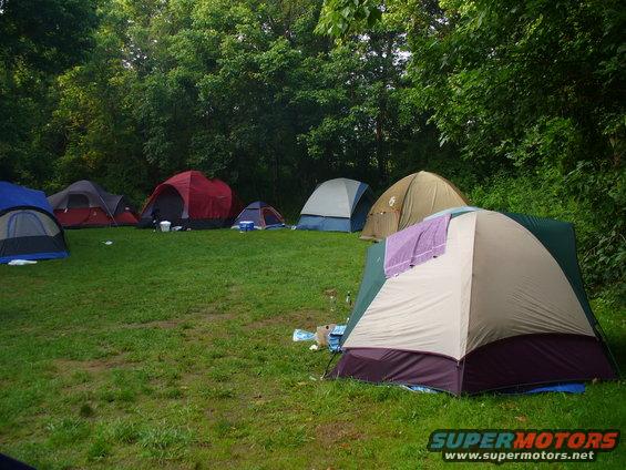 Several tents set up on a grassy field with trees in the background
