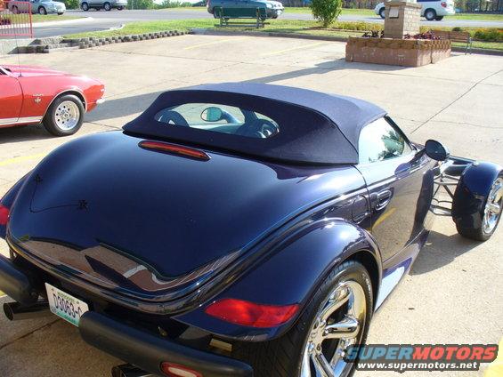 Dark blue convertible with a soft top, seen from the rear. A red classic car is to the left
