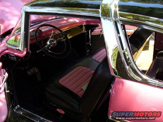 Interior view of a pink and black classic car, showing dashboard, steering wheel, and seats