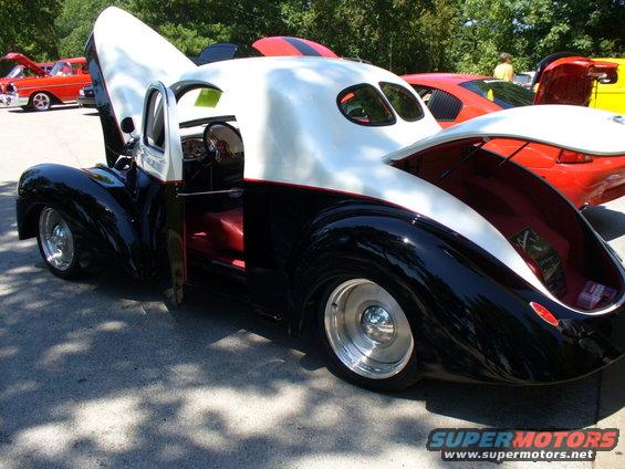 Black and white custom hot rod with red interior, hood and trunk open, parked at a car show