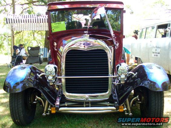 Maroon hot rod with skull headlights and custom fenders, front view. A green sign with '193' is visible on the windshield