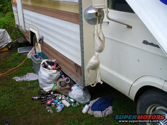 White RV with trash bags and beer cans on the ground, a bra hangs from the side mirror
