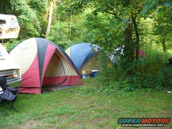 Campsite with multiple tents set up, a trailer, and a partial view of a vehicle's front end