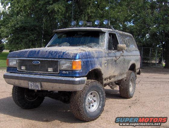 Mud-covered blue 1987 Ford Bronco with aftermarket lights on roof visor