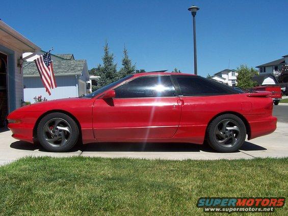1994 Ford Probe coupe, side view, red paint, tinted windows, parked in driveway with American flag visible