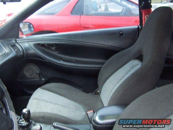 Interior view of a 1994 Ford Probe, showing the driver's seat and door panel. A red car is visible through the window