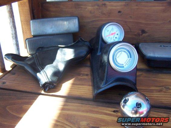 Car parts including a shift boot, gauges, and a shift knob on a wooden surface