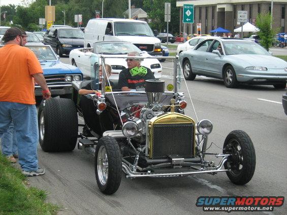 Black hot rod with exposed engine and gold grille, seen from the front