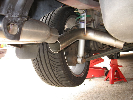 car's rear tire, exhaust pipe, shock absorber, and suspension components, with red jack stands underneath
