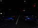 2003 Ford Mustang - Two blue Ford Mustangs are parked side-by-side in a lot at night, with headlights on.