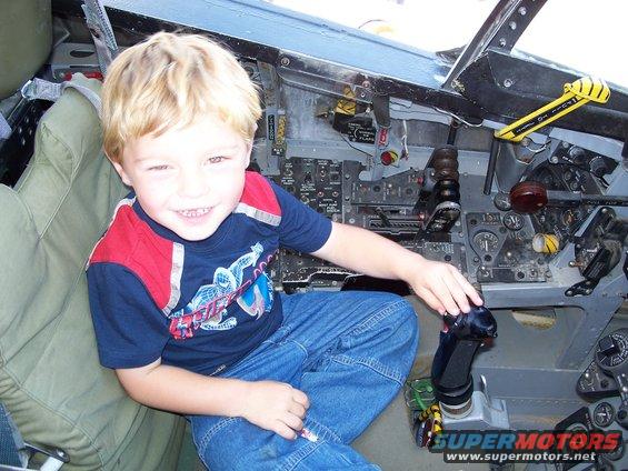 Child sits in an aircraft cockpit with many switches and levers