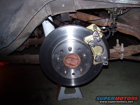 close-up of a vehicle's rear brake rotor and caliper assembly, supported by a jack stand