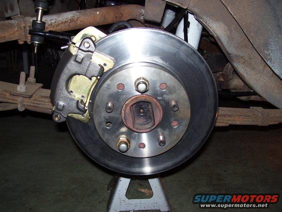 Car brake rotor and caliper assembly on a jack stand, showing suspension components and leaf springs