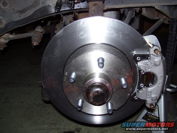 Close-up of a car's front brake rotor and caliper assembly, mounted on a jack stand