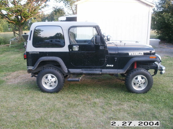Black Jeep Wrangler with a grey hardtop, parked on grass. "WRANGLER" is on the hood