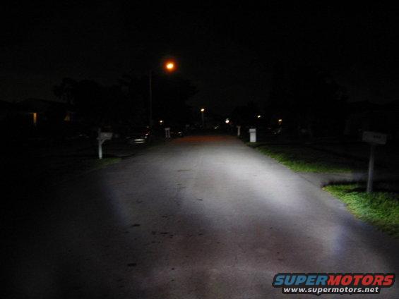 Headlights illuminate a dark suburban street at night. Supermotors.net logo visible