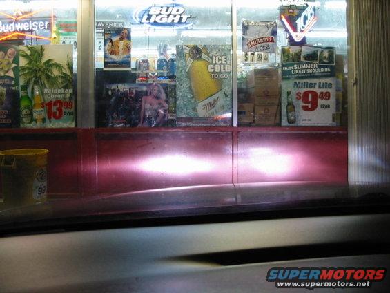 Car headlights illuminating a store window display with beer advertisements