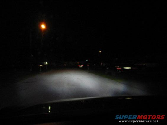 Dashboard view of headlights illuminating a dark street at night