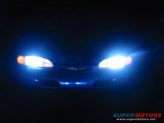 Blue 1995 Ford Thunderbird front with bright white headlights on